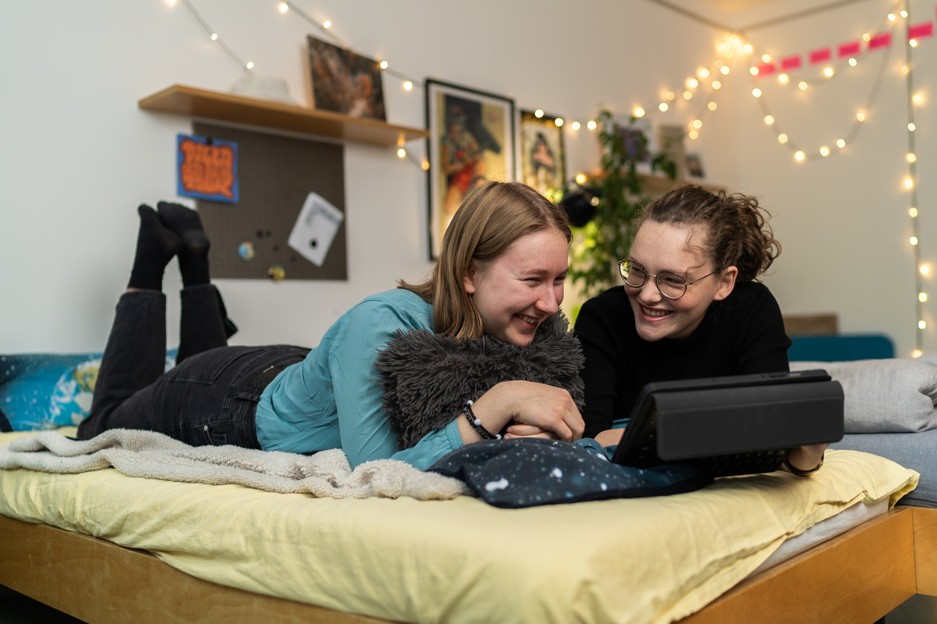 Mädchen liegen lächelnd auf einem Bett und schauen auf einem Tablet etwas an